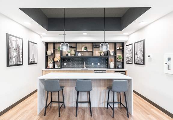A modern kitchen with a bar area and three grey bar stools.