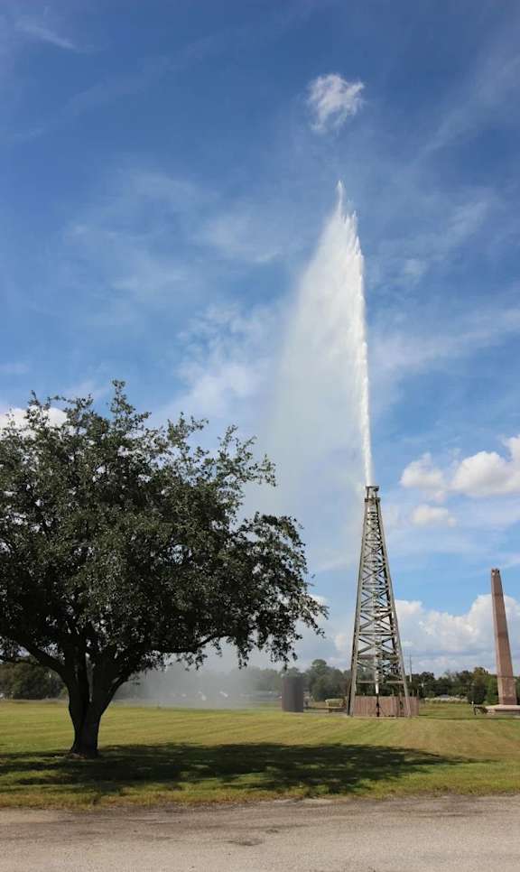 A large fountain shoots water into the air in front of a tall tower.