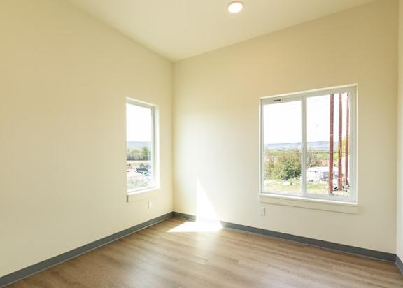 an empty living room with wood floors and two windows