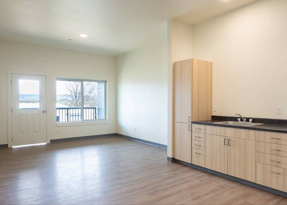 an empty living room with a kitchen and a door to a balcony