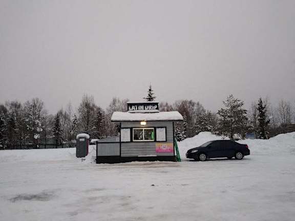 a black car parked in front of a food stand in the snow