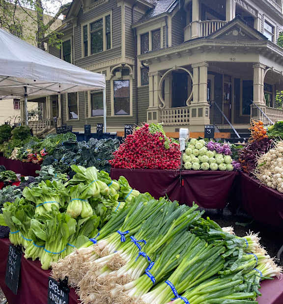 A market is set up in a park with people walking around and buying things.