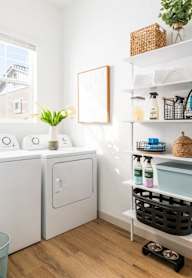 A laundry room with a washer and dryer, a basket of cleaning supplies, and a plant on the shelf.