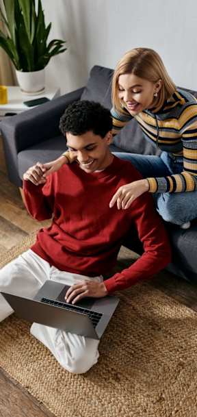 A man and woman are sitting on a couch with a laptop on the floor.