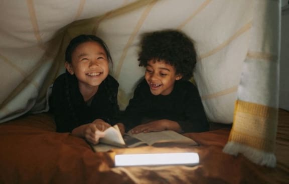 two young children reading a book in a tent