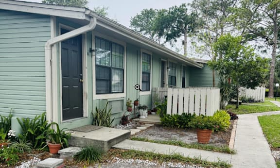 A green house with a white picket fence and a small garden in front.