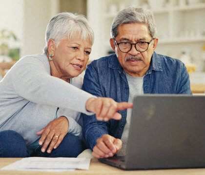 an older couple sitting on a couch looking at a laptop computer