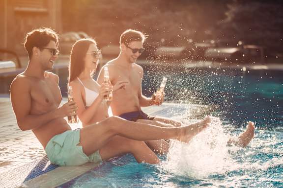 Three people are sitting on the edge of a pool with water splashing around them.