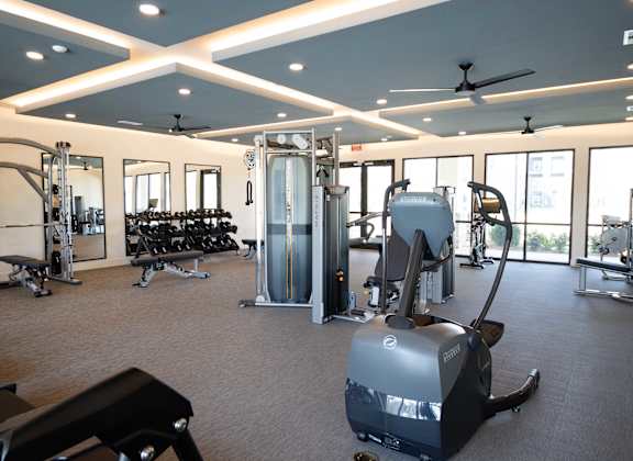 A gym with a variety of equipment including treadmills, weights, and a rowing machine at The Crest at South Point Apartments, McDonough, GA