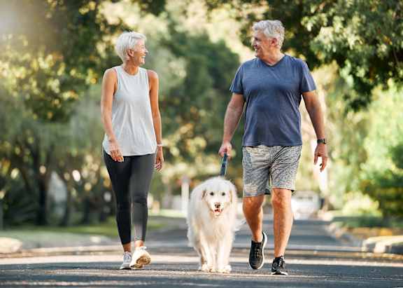 An older couple walking a dog in a park at The Laurel at Vintage Park 55+ Apartments, Tomball Texas