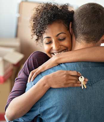 A couple hugging each other in a room with boxes in the background.