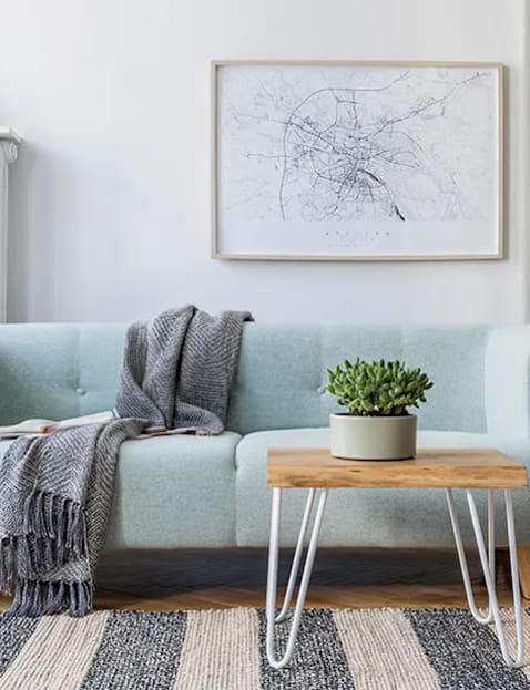 A living room with a blue couch, a small table with a plant, and a framed map on the wall.