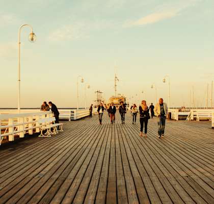 a group of people walking on a pier at sunset