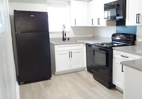 an empty kitchen with white cabinets and a black refrigerator