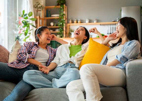 Three women laughing and sitting on a couch.