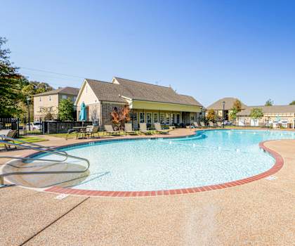 A large outdoor swimming pool with a red border and a small building in the background.