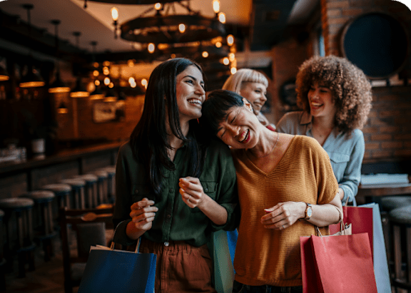 Women Laughing and Walking Together while Holding Shopping Bags