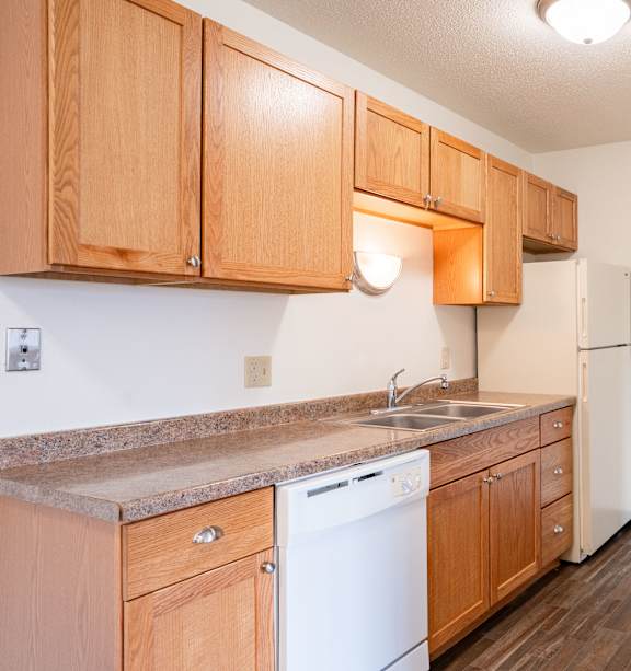 Bismarck, ND Stonefield Townhomes | Dining Room A kitchen with wooden cabinets and a white dishwasher. West Fargo, ND Saddlebrook Apartments