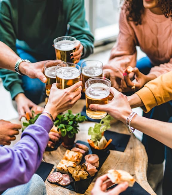 A group of people toasting with beer glasses at a table with food.