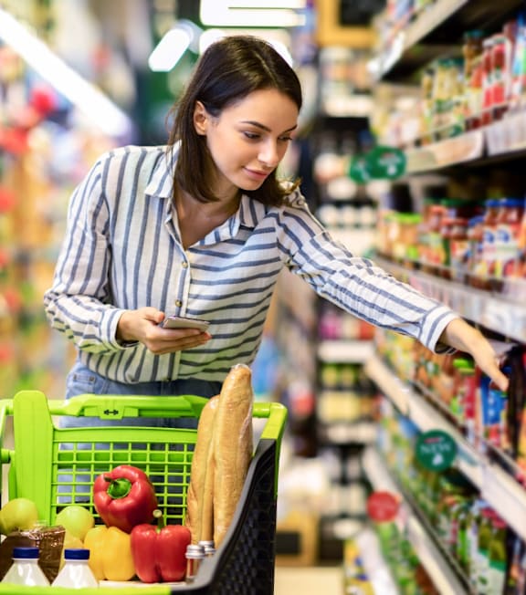 A woman is shopping in a grocery store with a basket full of fruits and vegetables.