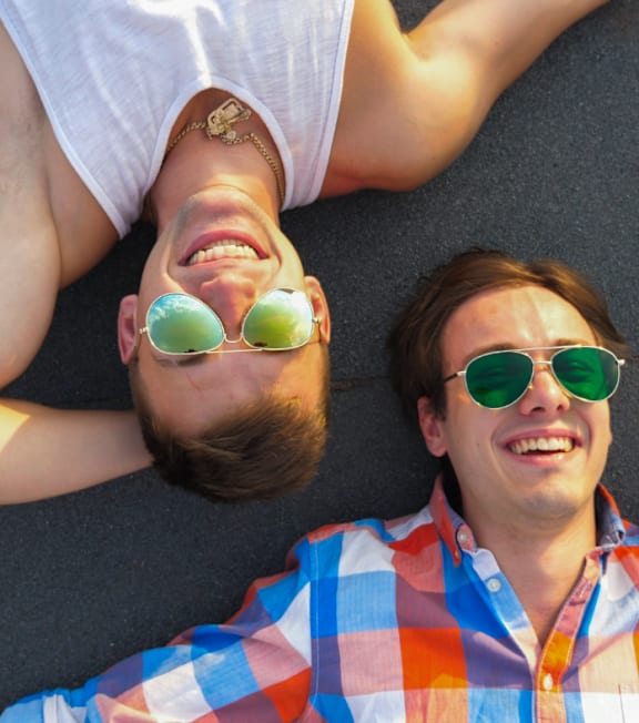 Two men wearing sunglasses and checkered shirts are lying down.