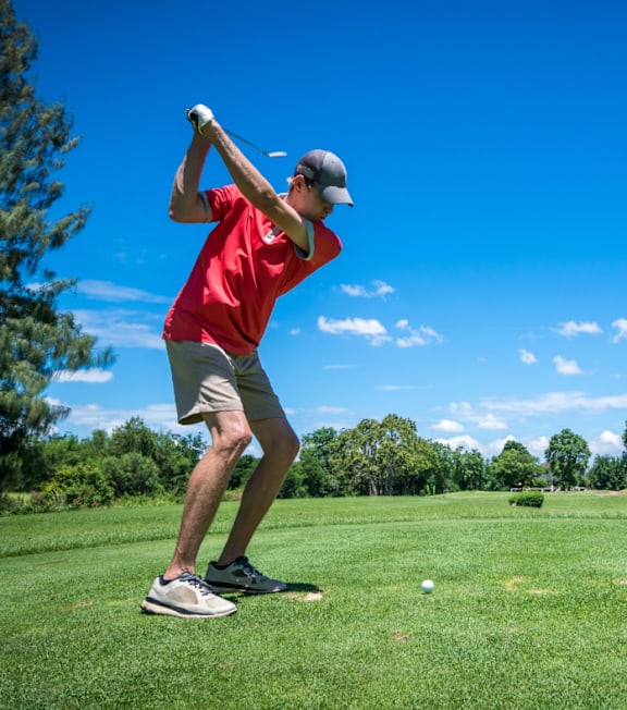 A man in a red shirt and grey shoes is playing golf.