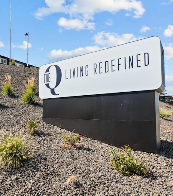 A sign that says "The Q Living Redefined" is displayed outdoors.