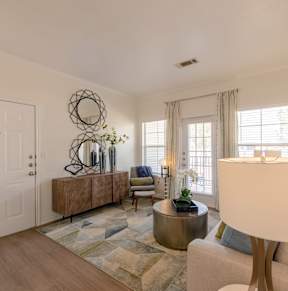 A well-lit living room with a white sofa, a round table, and a large mirror on the wall.