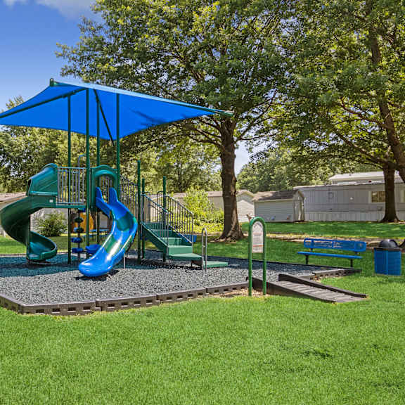 A playground with a blue umbrella and a green slide.