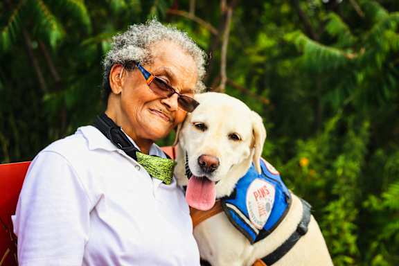an older woman poses with a yellow labrador retriever dog