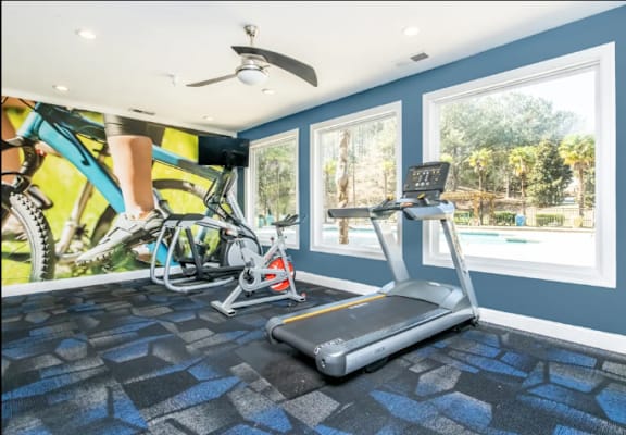 A room with a treadmill, a fan, and a wall mural of a person on a bike.