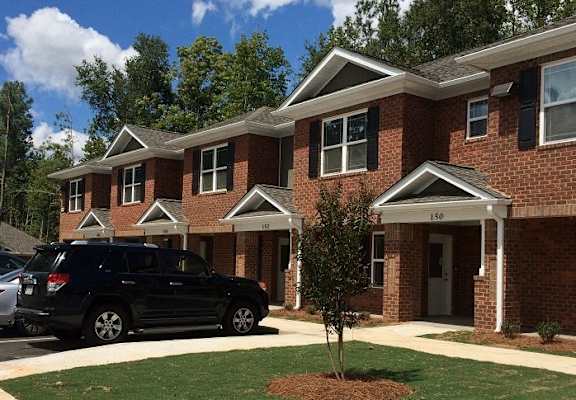 A black SUV is parked in front of a brick house with the number 150 on the front door.