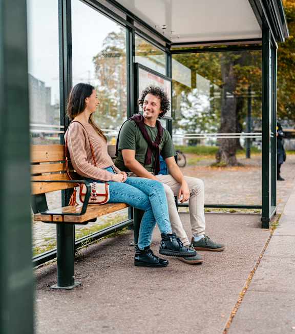 Two people sitting on a bench at a bus stop.