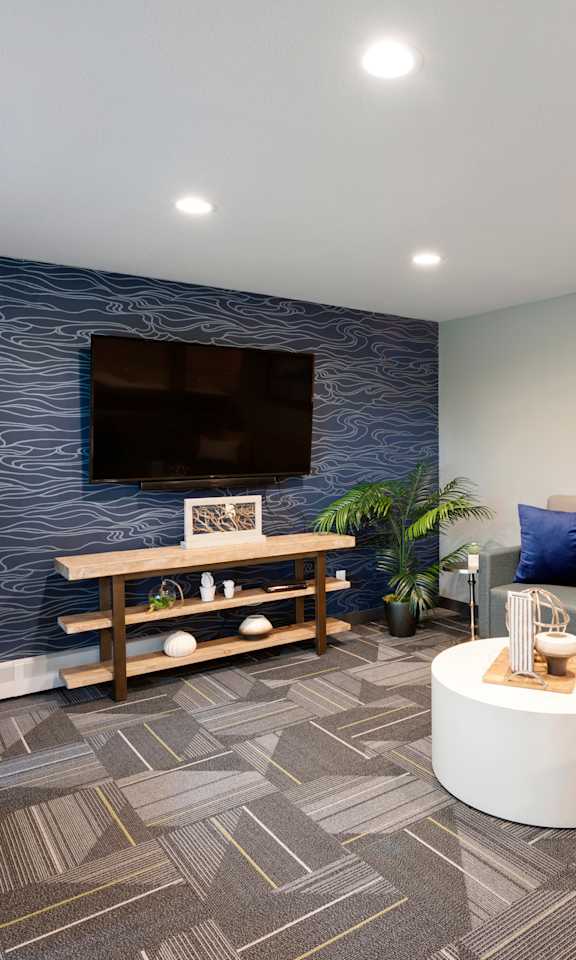 A modern living room with a grey carpet and a blue patterned wallpaper.