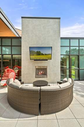 An outdoor fireplace with a comfortable U-shaped sofa and a TV near the clubhouse at Keva Flats. at Keva Flats, Exton, 19341