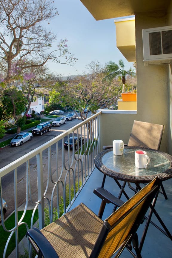 A table with a cup and a chair on a balcony overlooking a street.