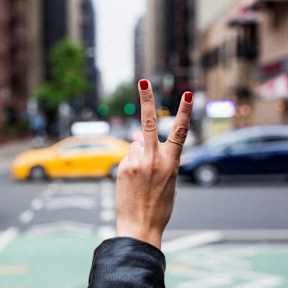 a hand holding up a peace sign on a city street