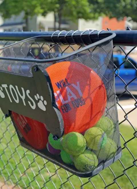 A mesh bag filled with sports balls is hanging on a fence.
