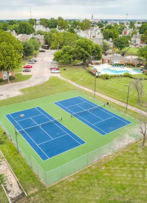 Two tennis courts surrounded by a green fence.