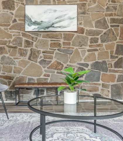 A grey chair sits in front of a stone wall with a plant on the table.