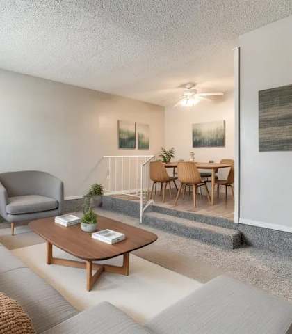 A living room with a grey couch, a grey armchair, a wooden coffee table, and a dining table with chairs.
