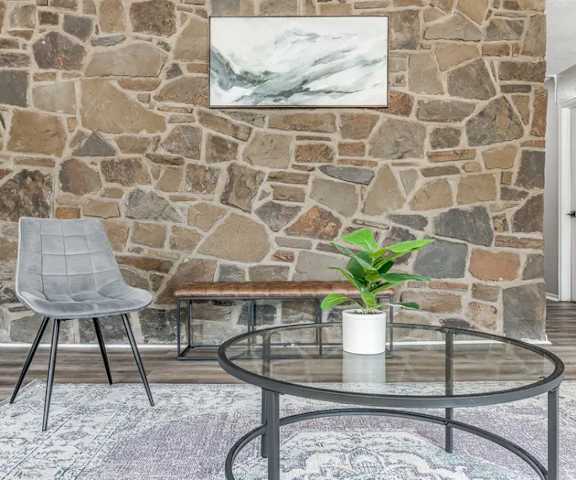 A grey chair sits in front of a stone wall with a plant on the table.