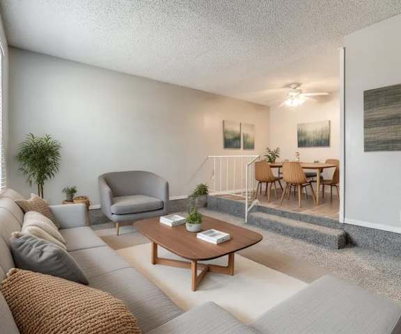 A living room with a grey couch, a grey armchair, a wooden coffee table, and a dining table with chairs.