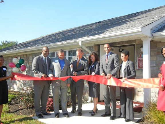 a group of people cutting a ribbon in front of a house