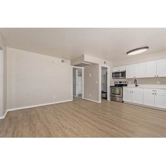 an open living room and kitchen with wood flooring and white cabinets