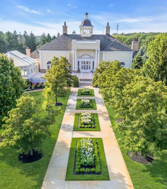 A large white building with a tower and a long pathway with flower beds on either side.