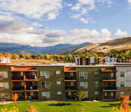 A view of apartment buildings with a car and trees in the foreground.