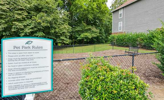 A sign in front of a fence lists the rules for a pet park.