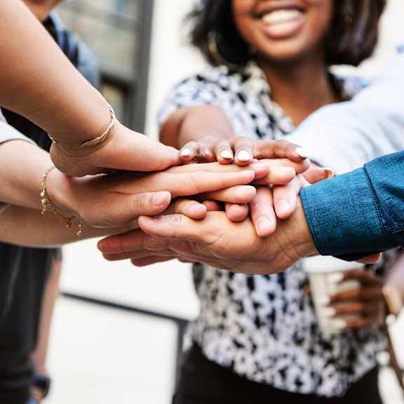 A group of people stacking their hands together in a show of unity.