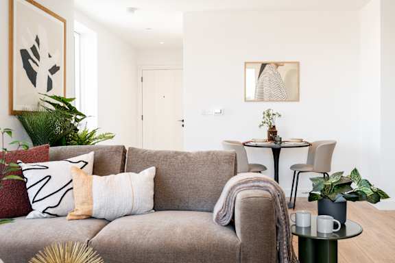 A living room with a grey couch, a small table with a plant and two cups, and a painting on the wall.